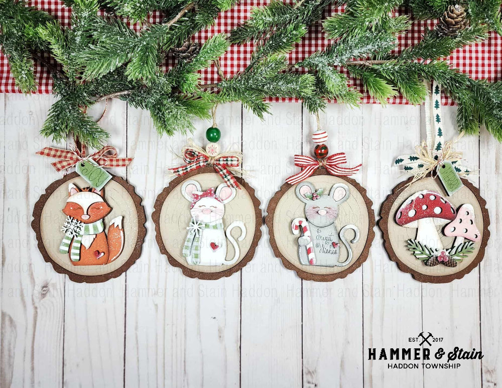 Forest Friends Christmas ornaments with animal designs on a wooden surface with greenery and a checkered cloth.