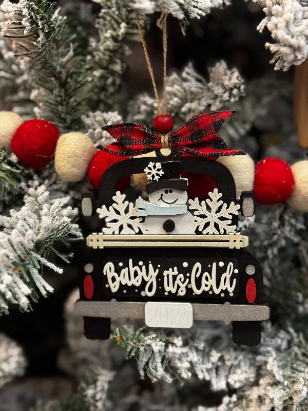 Decorative Christmas ornament with a truck and snowman, featuring the text 'Baby it's Cold', on a Christmas tree.