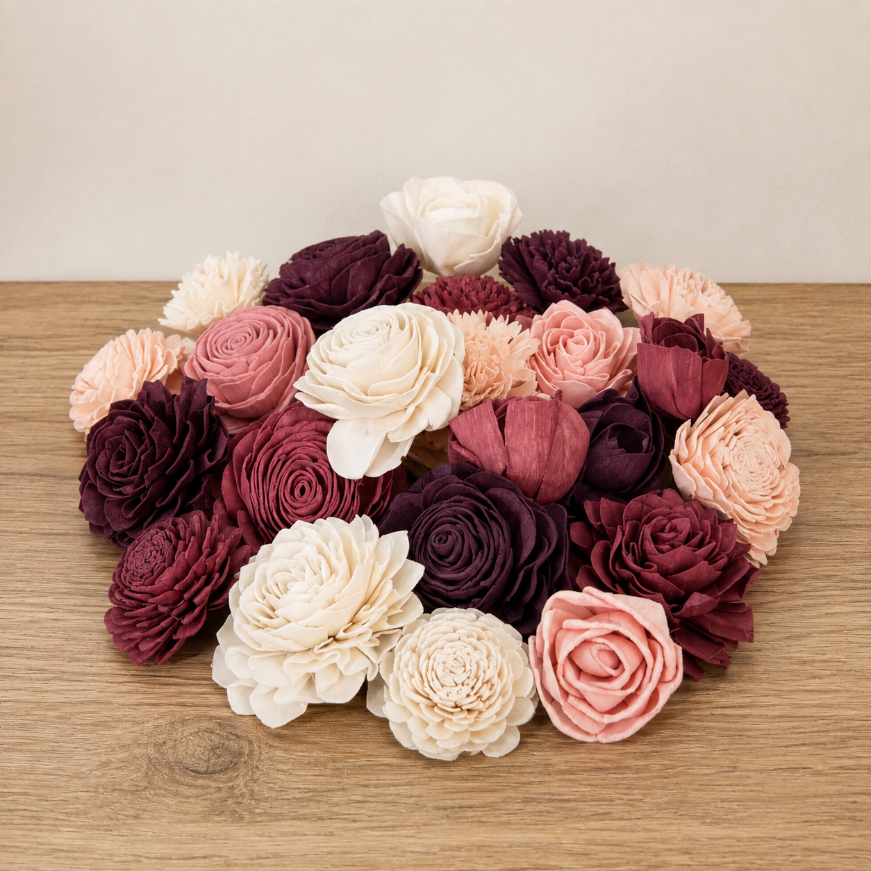 A cluster of artificial wood flowers in shades of burgundy, deep plum, blush pink, and cream used book vase flower arrangement.