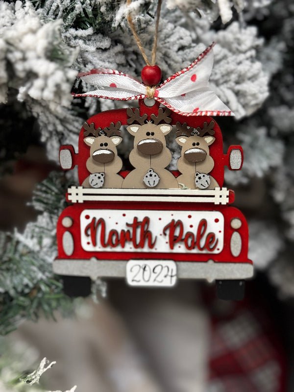 Christmas ornament with reindeer on a sleigh labeled 'North Pole and year' against a blurred Christmas tree background.