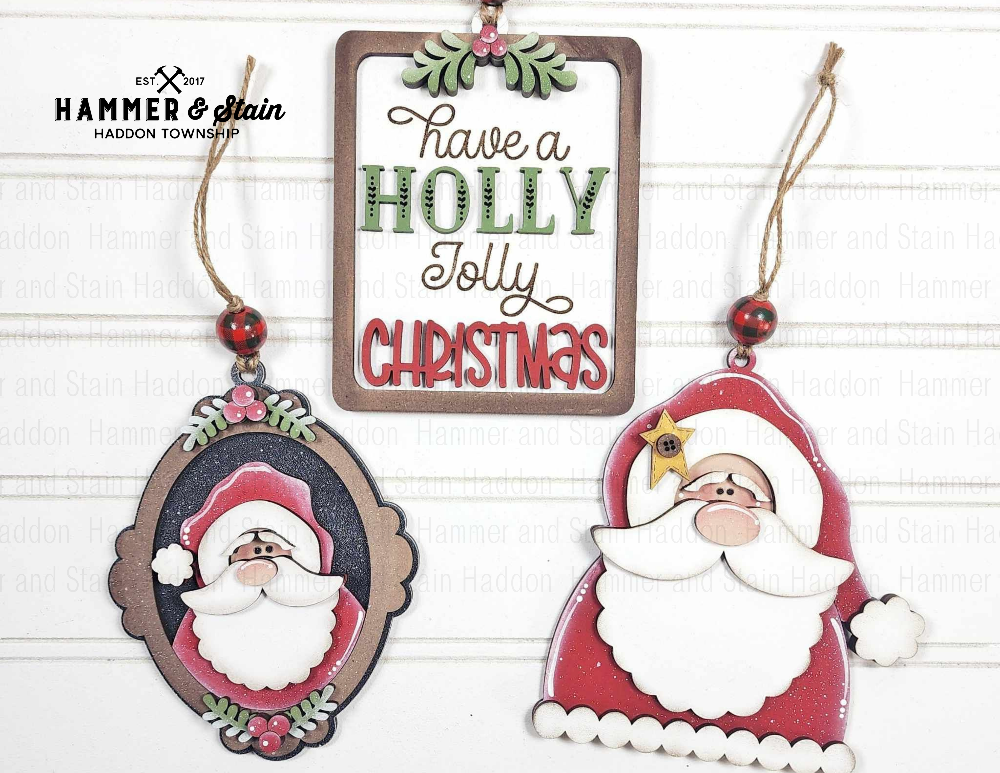 Three Christmas-themed ornaments with Santa Claus designs and a sign saying 'Have a Holly Jolly Christmas' on a white background.