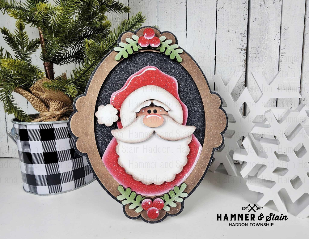 Decorative Christmas picture frame with a Santa Claus design, surrounded by festive elements on a wooden surface.